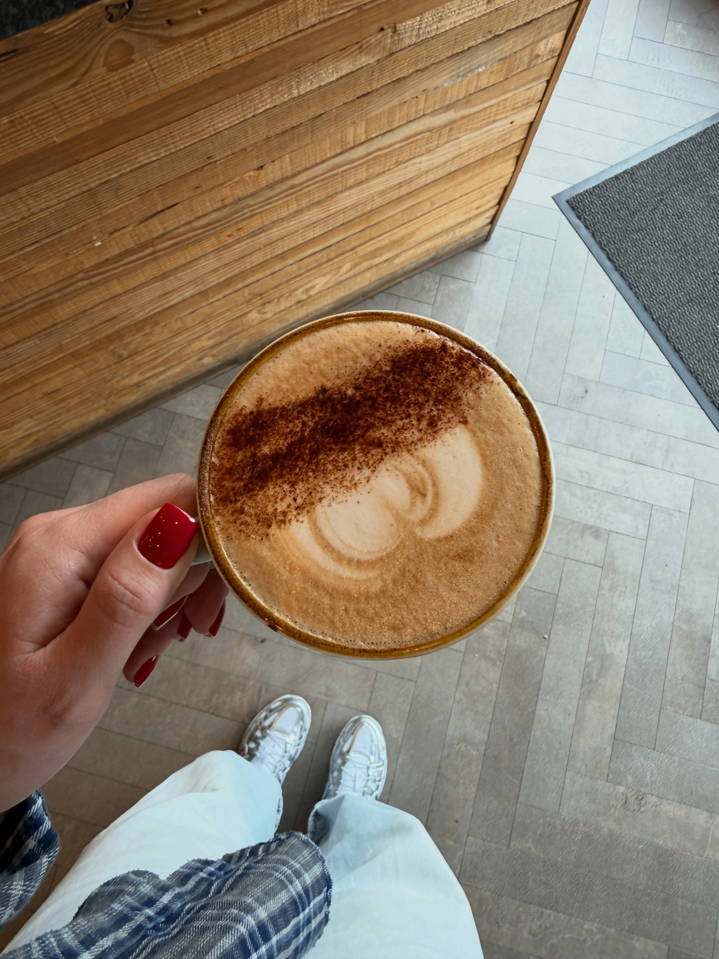 A ceramic mug of coffee on a sunlit wooden table surrounded by eucalyptus leaves